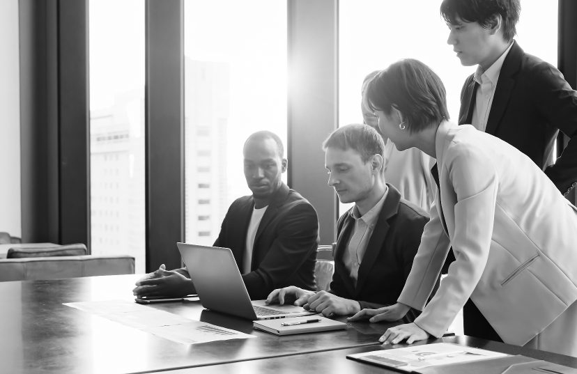 Black and white image of business professionals collaborating while working on a laptop in a modern office setting.