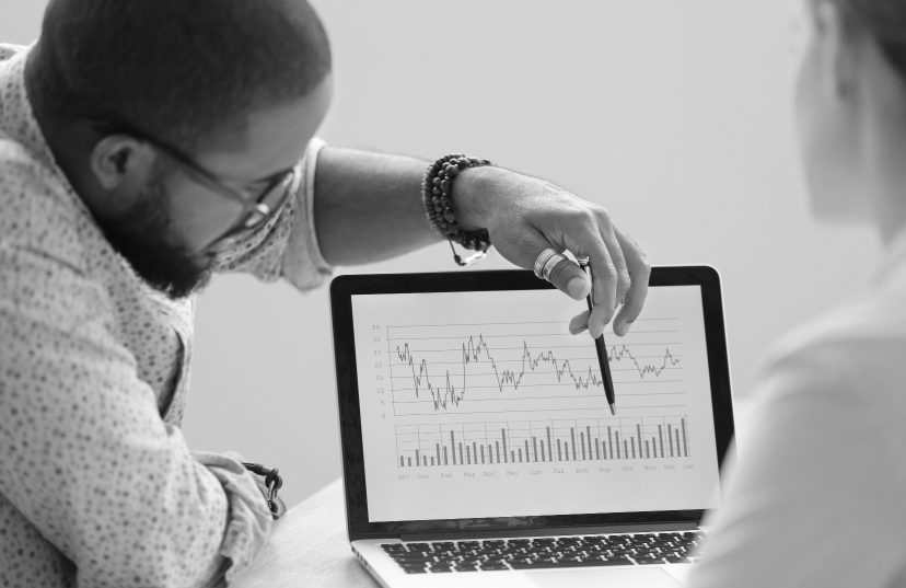 Two individuals examining a laptop screen displaying a graph, engaged in discussion about the data presented